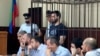 In this photo taken on Sunday, June 16, 2019, Abdulmumin Gadzhiev, the religious affairs editor of the independent weekly Chernovik, stands in a cage in a court room in Makhachkala, the Caspian Sea province of Dagestan, Russia, Sunday, June 16, 2019.