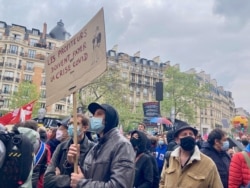 A protester holds a sign denouncing profiteers who have enriched themselves from the COVID crisis, in Paris, May 1, 2021. (Lisa Bryant/VOA)