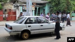 Burma police officers inspect a damaged vehicle at the scene of a small blast that happened close by the vehicle in Mandalay, July 22, 2013.