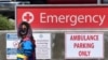 A woman wears a face covering while walking past a sign leading to the Emergency section at the Los Angeles County+USC Medical Center in Los Angeles, California, July 2, 2020.