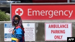 A woman wears a face covering while walking past a sign leading to the Emergency section at the Los Angeles County+USC Medical Center in Los Angeles, California, July 2, 2020.