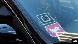 FILE - A ride share car displays Lyft and Uber stickers on its front windshield in downtown Los Angeles, Calif., Jan. 12, 2016.