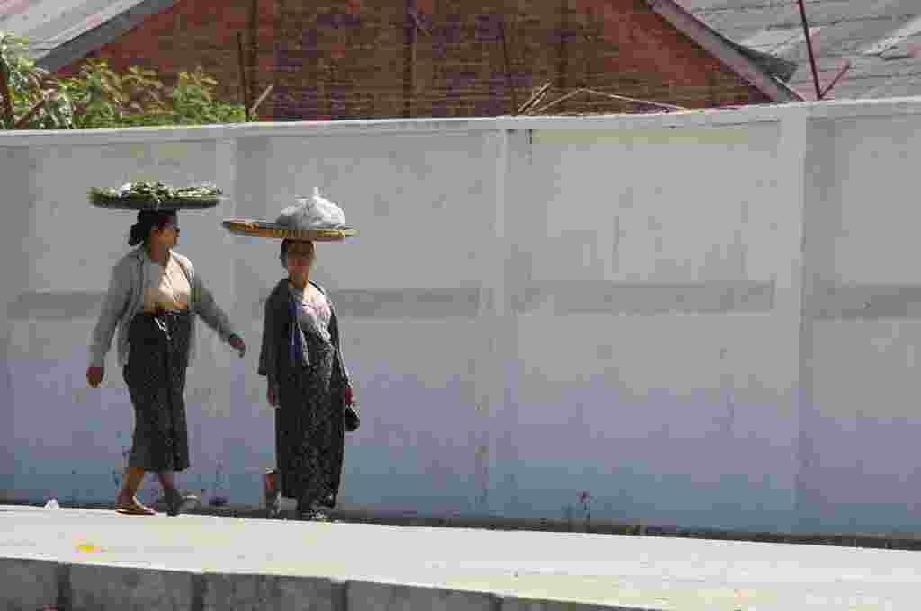 Dua perempuan membawa sayur-sayuran di kepala mereka saat berjalan di jalanan kota Rangoon (VOA-D.Schearf).