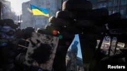 An anti-government protester is reflected in a mirror as he stands guard on a barricade that faces a cordon of riot police in Kyiv, Ukraine, Feb. 3, 2014.