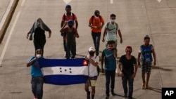 Migrantes caminan con una bandera hondureña, a lo largo de una carretera con la esperanza de llegar a los lejanos Estados Unidos, el miércoles 30 de septiembre de 2020.