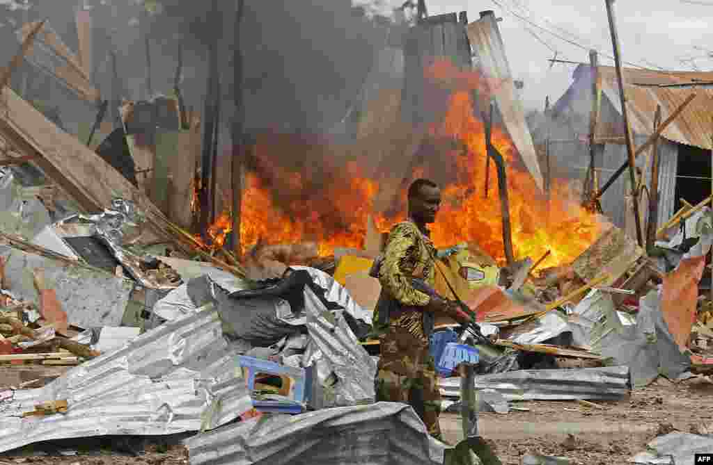 A Somali National Government (SNG) soldier walks past burning debris after a suspected suicide bomber rammed a car laden with explosives into an armored convoy of African Union troops in Mogadishu.