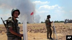 FILE - Turkish soldiers stand guard on the Turkish side of the border in Suruc as smoke rises in the background from the Syrian town of Kobani. 