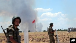 Turkish soldiers stand guard on the Turkish side of the border in Suruc, Turkey, June 26, 2015, as smoke rises in the background. 