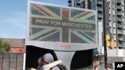 FILE - A couple embraces under a billboard in Manchester, England, the day after the suicide attack at an Ariana Grande concert that left more than 22 people dead, May 23, 2017. 