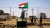 FILE - A Sudanese protester holds a national flag as he stands on a barricade along a street, in Khartoum, Sudan, June 5, 2019. 