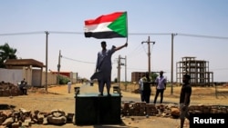 FILE - A Sudanese protester holds a national flag as he stands on a barricade along a street, in Khartoum, Sudan, June 5, 2019. 
