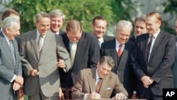 In this Oct. 22, 1986, file photo, lawmakers watch closely as President Ronald Reagan signs into law a landmark tax overhaul on the South Lawn of the White House in Washington.