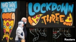 La gente pasa junto a un mural en las ventanas de un restaurante de pizza cerrado en medio del brote de la enfermedad del coronavirus en Manchester, Reino Unido, el 22 de febrero de 2021.