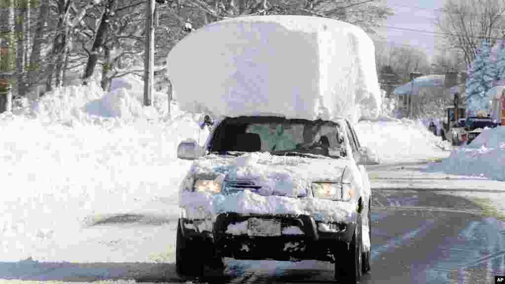 Un véhicule, avec une grande partie de la neige au-dessus, circule le long de la route 20 après été dégagée de l'épaisse chute de neige tombée à&nbsp;Lancaster, NY, mercredi 19 novembre 2014.