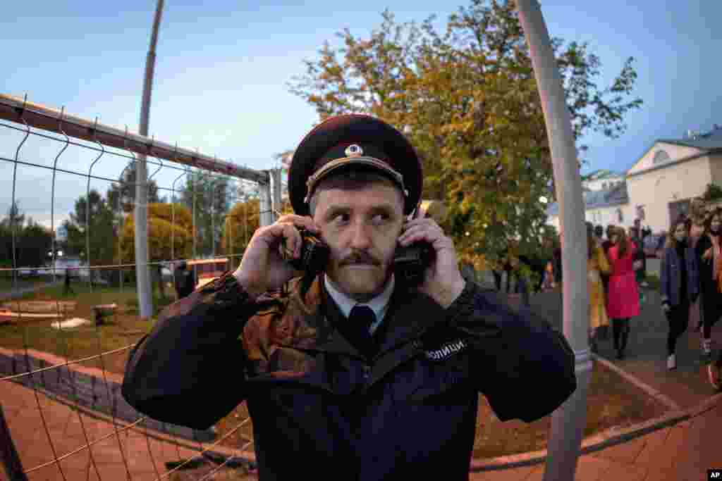 A police officer speaks on two walkie talkies as demonstrators gather to protest plans to construct a cathedral in a park in Yekaterinburg, Russia.