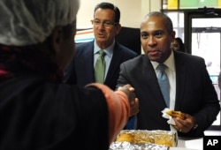 FILE - Deval Patrick, right, then Massachusetts' governor, shakes hands with bakery employees as then-Gov. Dannel P. Malloy, center, looks on, during a campaign stop, Oct. 10, 2014, in Hartford, Conn.