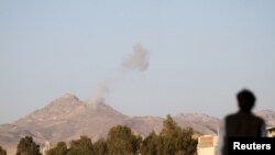Un hombre mira un columna de humo que se eleva de cuarteles militares en las montañas, tras un ataque aéreo cerca de Saná, el lunes, 30 de marzo, de 2015. 
