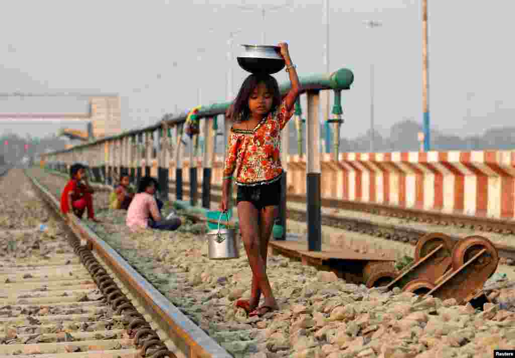 A girl carries water in a pot and a bucket on the outskirts of Agartala, India.