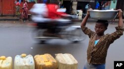 FILE - A young vendor walks past jerrycans of water for sale in central Monrovia, Liberia. Improvements in road maintenance are a major element of the MCC.