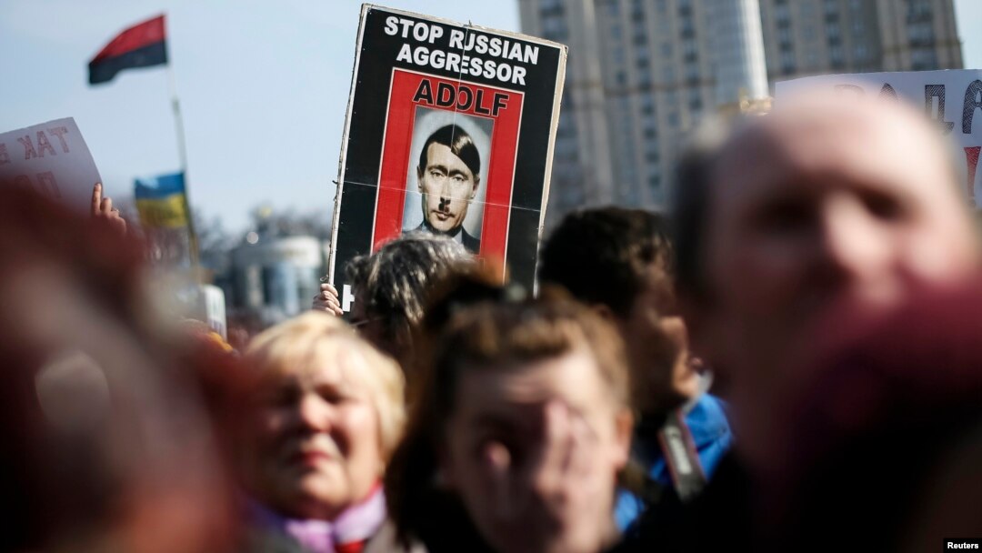 People hold a sign depicting Russian President Vladimir Putin as Adolf Hitler as they attend a unity rally at Independence Square, in Kyiv, Ukraine, March 23, 2014.