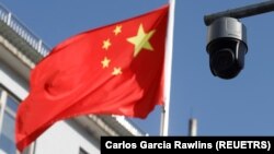 A security camera overlooking a street is pictured next to a nearby flag of China in Beijing, China on November 25, 2021. (REUTERS/Carlos Garcia Rawlins)