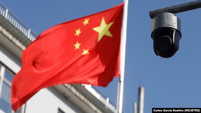 A security camera overlooking a street is pictured next to a nearby flag of China in Beijing, China on November 25, 2021. (REUTERS/Carlos Garcia Rawlins)