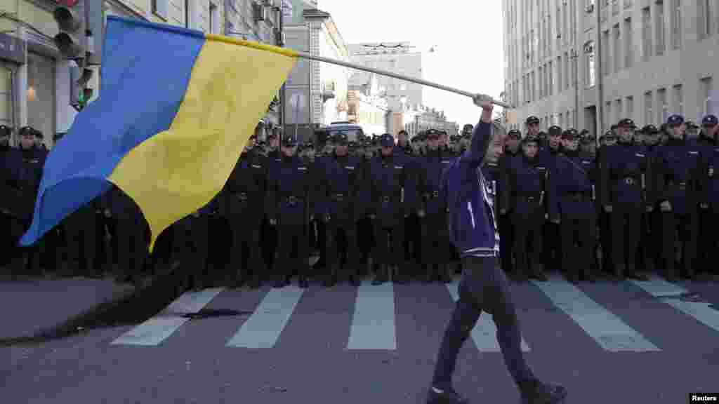 A man with a Ukrainian flag walks past riot police standing guard during an anti-war rally in Moscow, Sept. 21, 2014. 