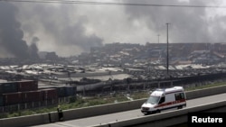 A firefighter watches smoke rising from a highway next to an ambulance, near the site of the explosions at the Binhai new district, Tianjin, August 13, 2015.