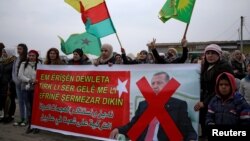 People hold flags and carry a banner reading, "We condemn and denounce the attacks of the Turkish government against our people in Afrin," during a protest against Turkish attacks on Afrin, in Hasaka, Syria, Jan. 18, 2018. 