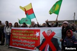 FILE - People hold flags and carry a banner reading, "We condemn and denounce the attacks of the Turkish government against our people in Afrin," during a protest against Turkish attacks on Afrin, in Hasaka, Syria, Jan. 18, 2018.