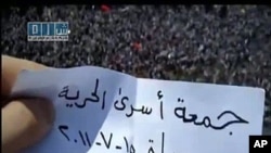 An image taken from footage uploaded on YouTube by the Shams News Network (SNN) shows a Syrian anti-government protester holding a piece of paper which says in Arabic 'Friday of Prisoner Freedom, Hama, July 15, 2011' on a rooftop above thousands of people