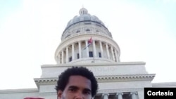 El artista Luis Manuel Otero Alcántara posa con la bandera cubana desde el Capitolio de La Habana, actual sede del parlamento de Cuba. {Foto cortesía MSI]