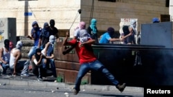 Seorang warga Palestina melemparkan batu ke arah polisi Israel dalam bentrokan di Shuafat, wilayah sub-urban Arab di Yerusalem (2/7).