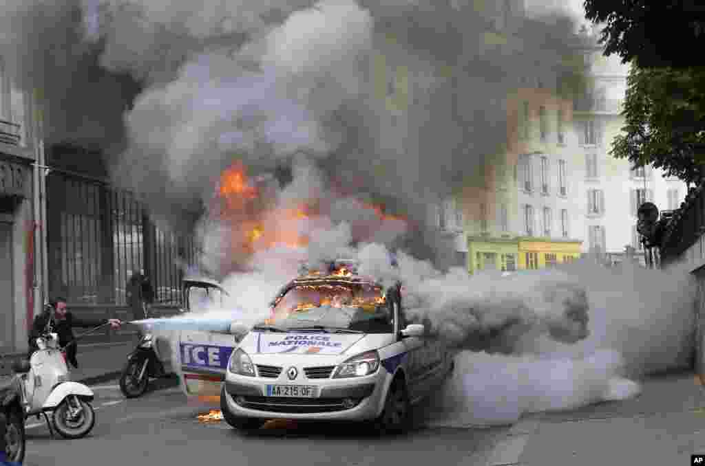 A man tries to pull out a fire on a police car during during a demonstration against police violence and against a labor reform in Paris, France.