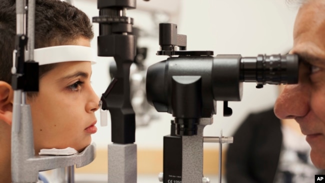 In this file photo, Dr. Albert Maguire (R), at the Children's Hospital of Philadelphia, checks the eyes of Misa Kaabali, 8, who was 4-years-old when he received his gene therapy treatment, Oct. 4, 2017.