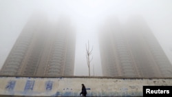 FILE - A woman wearing a mask walks past buildings on a polluted day in Handan, Hebei province, China, Jan. 12, 2019. China is reportedly the world's top emitter of greenhouse gases.