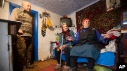 Kateryna Shklyar, right, speaks to The Associated Press as her husband, Dmytro, left, and Halyna Moroka gather near her at her house in the village of Nevelske in eastern Ukraine, on Dec. 10, 2021.