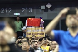 A fan drapes a Chinese national flag over an NBA banner during a preseason NBA basketball game between the Brooklyn Nets and Los Angeles Lakers at the Mercedes Benz Arena in Shanghai, China, Oct. 10, 2019.