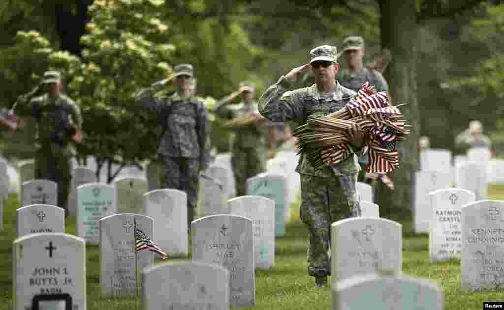 Soldiers salute as "Taps" is played during a military funeral nearby as they were placing flags on graves at Arlington National Cemetery in Virginia, May 23, 2013.