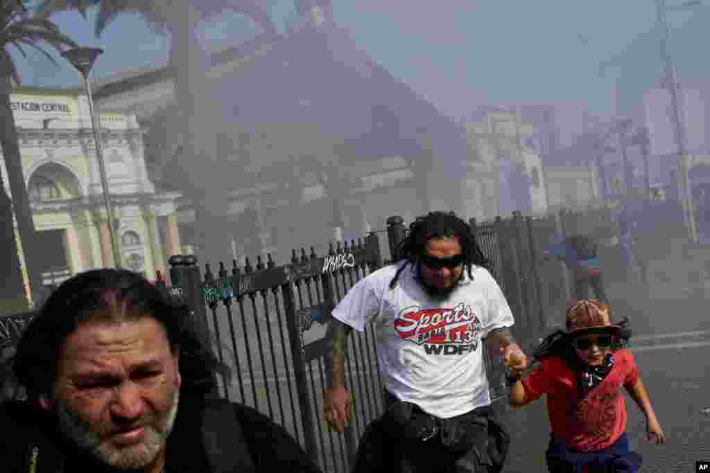 A father and his daughter run from a scene where protesters and riot police clash during the May Day march that turned violent, in Santiago, Chile, May 1, 2018.