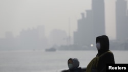FILE - People wear protective masks near the Bund during a polluted day in Shanghai, China.