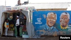 FILE - Youths stand outside a makeshift shop near murals of former South African president and anti-apartheid hero Nelson Mandela in Soweto, Johannesburg, South Africa.