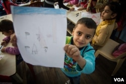 A child shows off his latest drawing as part of a class run by NGO Najda Now. The classes allow refugee children the chance to depict their dreams and fears through pictures, Dec. 4, 2015. (J. Owens/VOA)