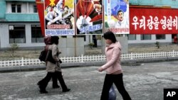 North Koreans walk past posters reading "Forward to the ultimate victory under the leadership of the great party!" on March 19, 2013 on a street in Phyongchon District in Pyongyang.