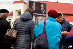 People stand on the street with a billboard depicting Ukraine's President Petro Poroshenko and Russian President Vladimir Putin looking at each other om the background, in Kyiv, Ukraine, April 17, 2019.