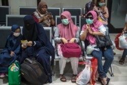 Penumpang yang mengenakan masker di tengah kekhawatiran penyebaran COVID-19 menunggu untuk naik kereta di stasiun kereta di Surabaya pada 15 Maret 2020. (Foto: Juni Kriswanto/AFP)