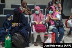 Penumpang yang mengenakan masker di tengah kekhawatiran penyebaran COVID-19 menunggu untuk naik kereta di stasiun kereta di Surabaya pada 15 Maret 2020. (Foto: Juni Kriswanto/AFP)