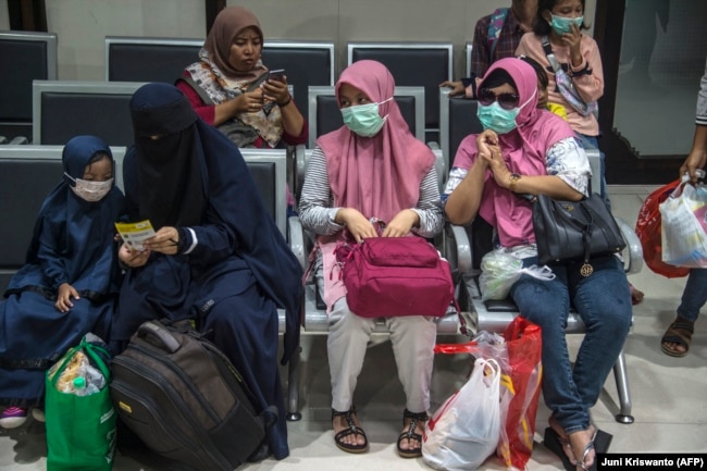 Penumpang yang mengenakan masker di tengah kekhawatiran penyebaran COVID-19 menunggu untuk naik kereta di stasiun kereta di Surabaya pada 15 Maret 2020. (Foto: Juni Kriswanto/AFP)