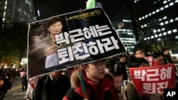 FILE - A South Korean protester carries a placard showing images of South Korean President Park Geun-hye and Choi Soon-sil, top left, during a rally calling for Park to step down, Nov. 2, 2016, in Seoul, South Korea. 