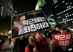A South Korean protester carries a placard showing images of South Korean President Park Geun-hye and Choi Soon-sil, top left, during a rally calling for Park to step down, Nov. 2, 2016, in Seoul, South Korea.